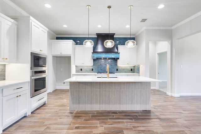 kitchen featuring a center island with sink, decorative backsplash, ornamental molding, decorative light fixtures, and white cabinetry