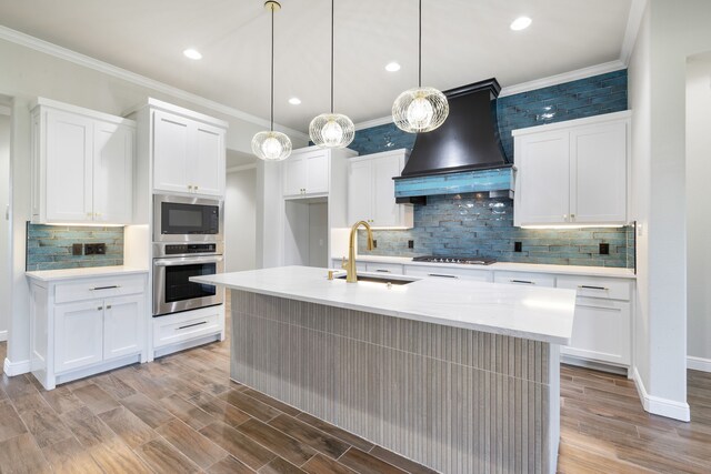 kitchen featuring white cabinets, custom range hood, stainless steel appliances, and a center island with sink