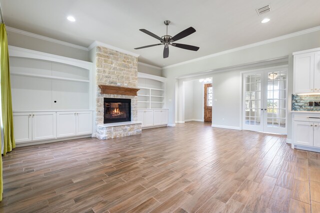 unfurnished living room with ceiling fan, a stone fireplace, built in features, and crown molding