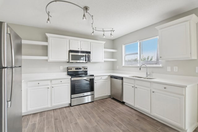 kitchen featuring sink, light hardwood / wood-style flooring, a textured ceiling, white cabinets, and appliances with stainless steel finishes