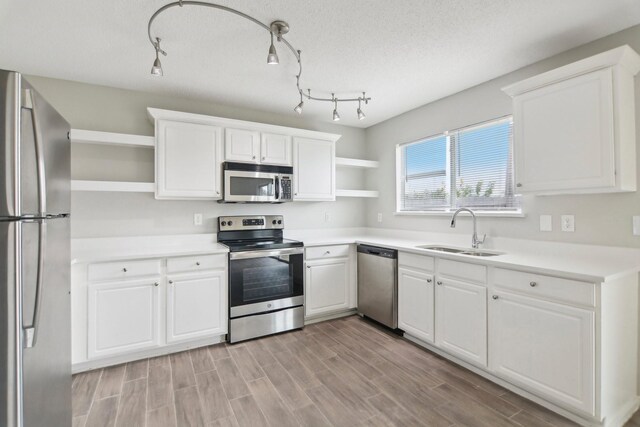 kitchen featuring sink, light hardwood / wood-style flooring, a textured ceiling, white cabinets, and appliances with stainless steel finishes