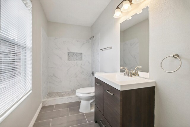 bathroom with tile patterned flooring, vanity, toilet, and a tile shower