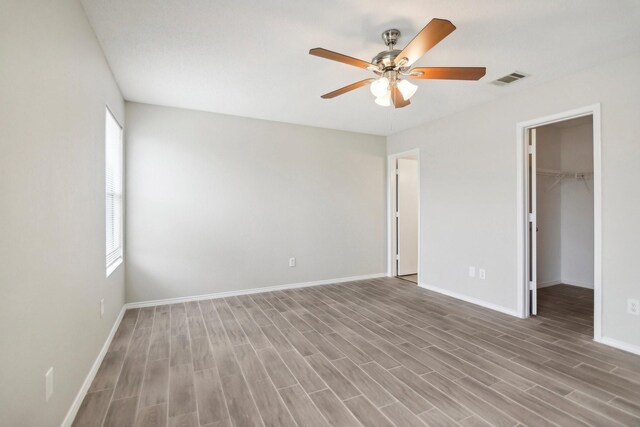 unfurnished bedroom with wood-type flooring, a walk in closet, a closet, and ceiling fan