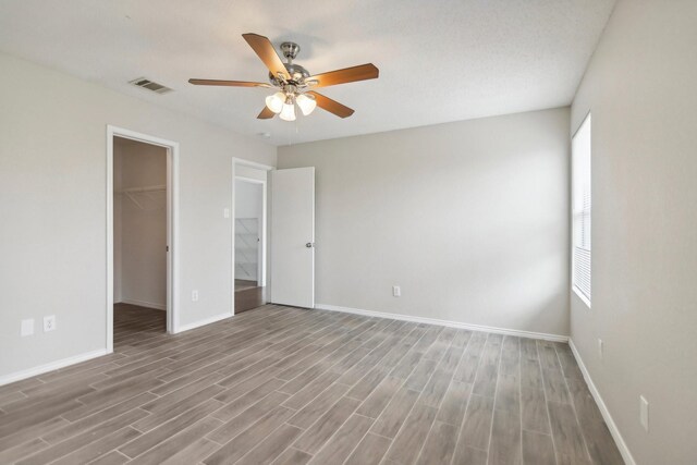 unfurnished bedroom with light wood-type flooring, a walk in closet, a textured ceiling, ceiling fan, and a closet