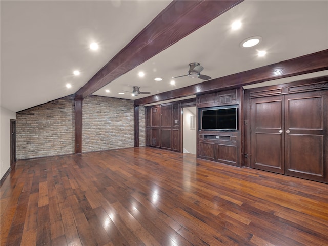 unfurnished living room with lofted ceiling with beams, ceiling fan, dark wood-type flooring, and brick wall