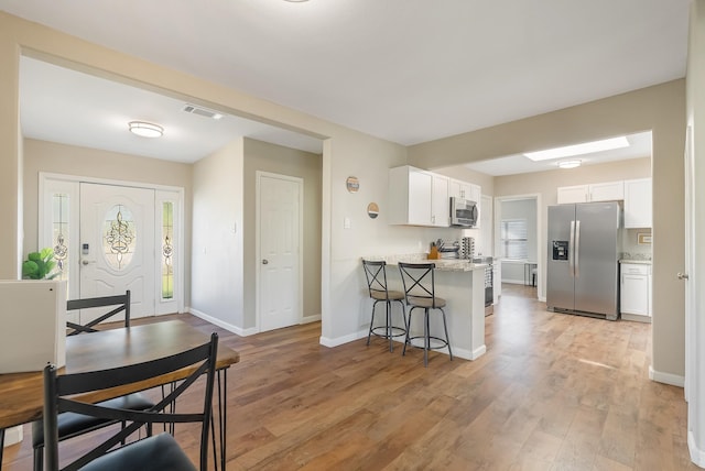 kitchen with a kitchen bar, appliances with stainless steel finishes, kitchen peninsula, light hardwood / wood-style flooring, and white cabinets