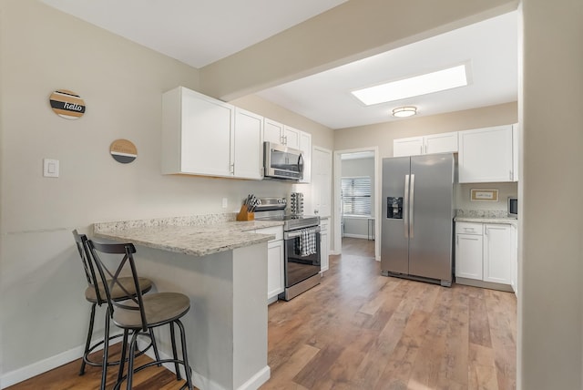 kitchen with a kitchen breakfast bar, white cabinets, stainless steel appliances, and light hardwood / wood-style floors