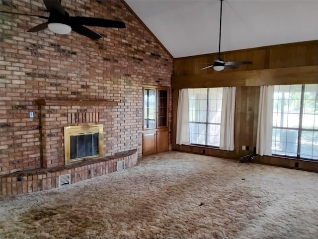 unfurnished living room featuring a brick fireplace, carpet, ceiling fan, and wooden walls