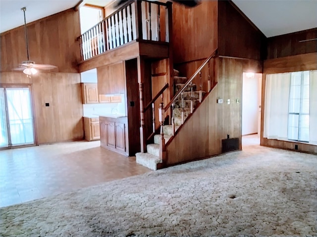 unfurnished living room with ceiling fan, high vaulted ceiling, and wooden walls