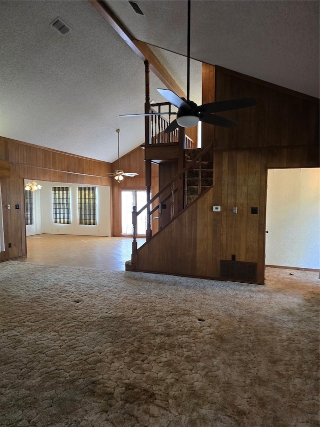 unfurnished living room with wooden walls, beamed ceiling, high vaulted ceiling, and ceiling fan