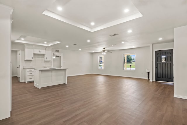 unfurnished living room with dark hardwood / wood-style flooring, a raised ceiling, and ceiling fan