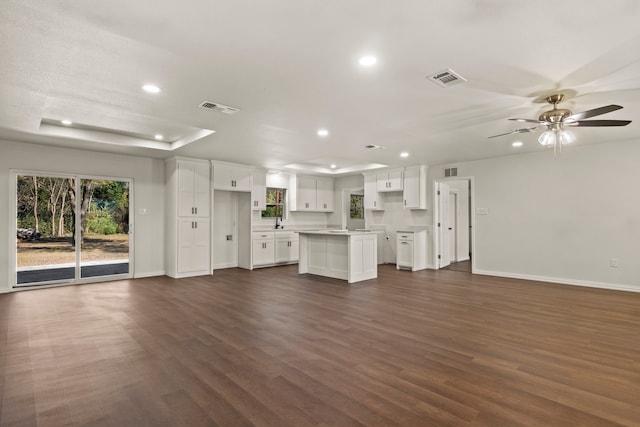 unfurnished living room featuring ceiling fan, sink, dark wood-type flooring, and a tray ceiling