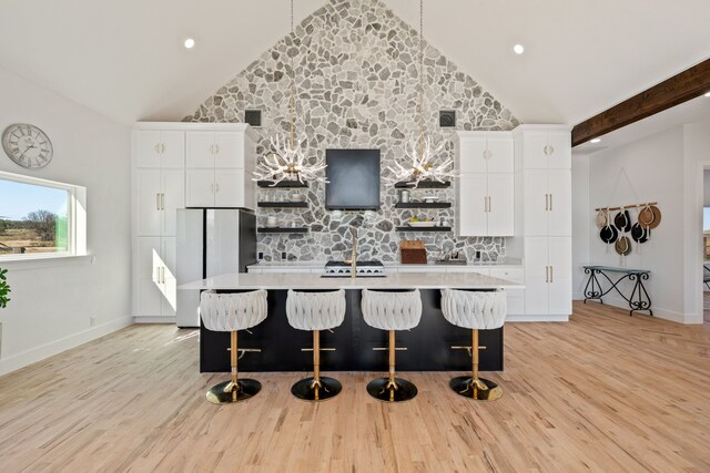 kitchen featuring a kitchen bar, light wood-type flooring, a kitchen island with sink, high vaulted ceiling, and white cabinets