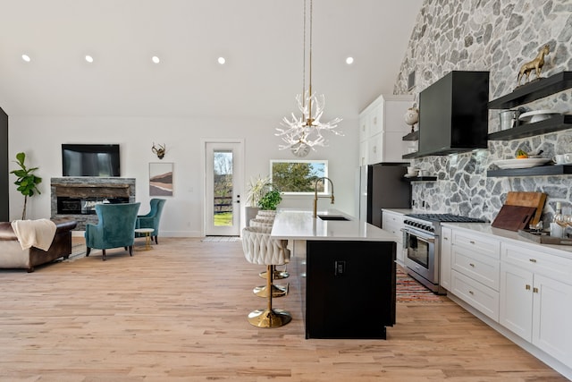 kitchen with exhaust hood, a center island with sink, light wood-type flooring, decorative light fixtures, and stainless steel appliances