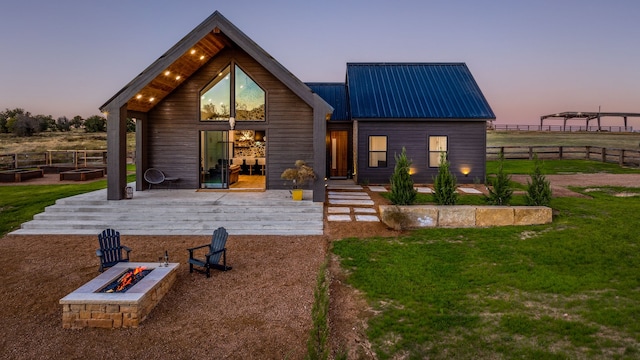 back house at dusk featuring an outdoor fire pit and a lawn