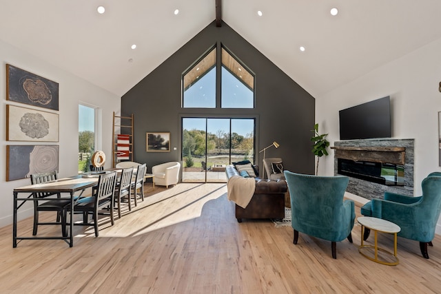 living room featuring a stone fireplace, high vaulted ceiling, and light hardwood / wood-style floors