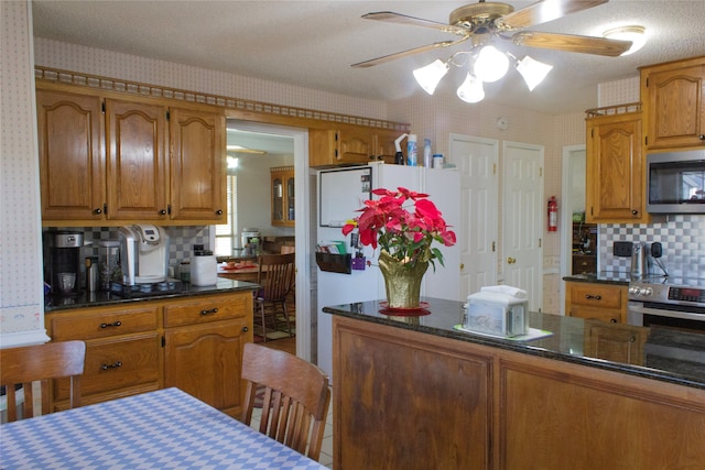 kitchen featuring ceiling fan, dark stone counters, a textured ceiling, decorative backsplash, and appliances with stainless steel finishes