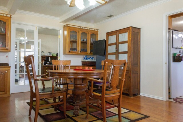 dining area featuring beam ceiling, a textured ceiling, light hardwood / wood-style flooring, and crown molding