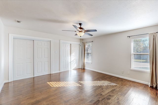 unfurnished bedroom featuring ceiling fan, dark hardwood / wood-style floors, a textured ceiling, and multiple closets