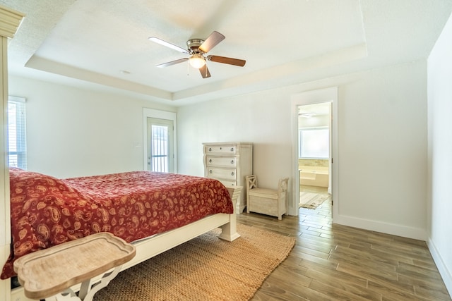 bedroom with ceiling fan, wood-type flooring, ensuite bathroom, and a tray ceiling