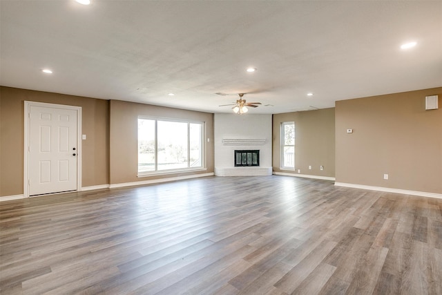 unfurnished living room with a brick fireplace, ceiling fan, a healthy amount of sunlight, and light wood-type flooring