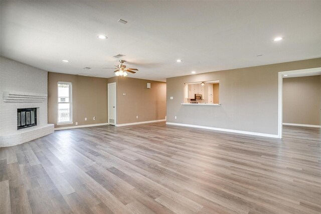 unfurnished living room with ceiling fan, light wood-type flooring, and a brick fireplace