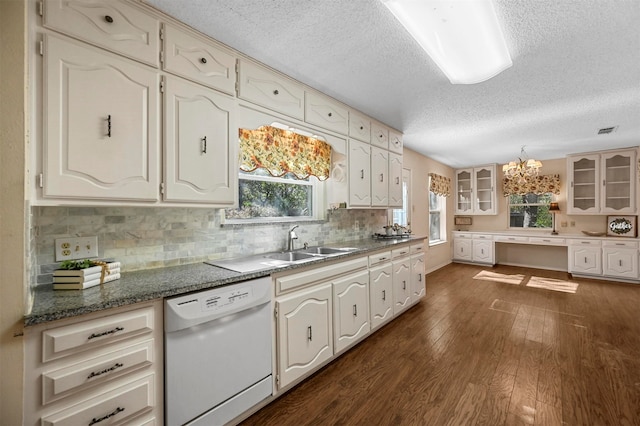 kitchen with dishwasher, backsplash, an inviting chandelier, dark stone countertops, and dark hardwood / wood-style flooring