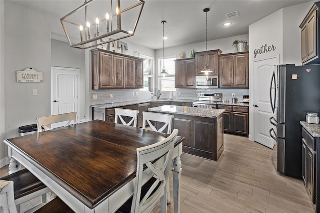 kitchen with dark brown cabinets, stainless steel appliances, pendant lighting, a chandelier, and a center island