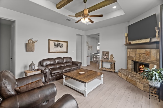 living room featuring ceiling fan, light hardwood / wood-style floors, and a stone fireplace