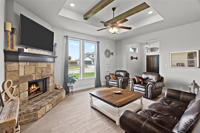 living room with a stone fireplace, a raised ceiling, ceiling fan, beamed ceiling, and light hardwood / wood-style floors