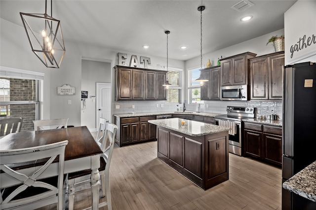 kitchen featuring light wood-type flooring, dark brown cabinets, stainless steel appliances, decorative light fixtures, and a kitchen island