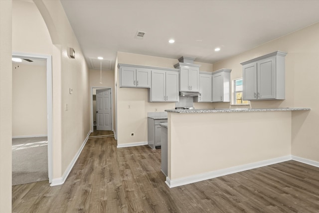 kitchen featuring light stone countertops, kitchen peninsula, gray cabinetry, ceiling fan, and hardwood / wood-style flooring