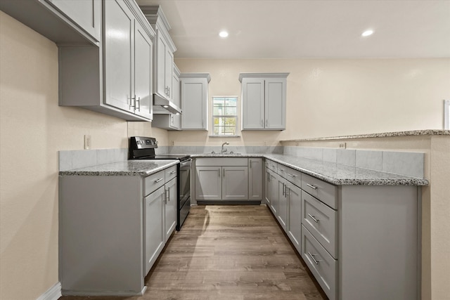 kitchen with sink, black electric range, hardwood / wood-style flooring, gray cabinets, and light stone counters