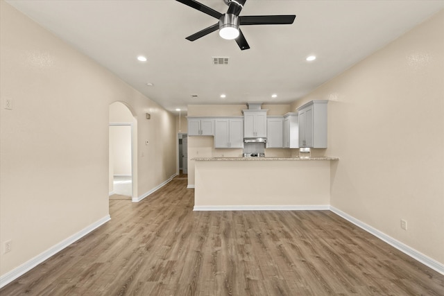 kitchen featuring white cabinets, ceiling fan, light stone countertops, light hardwood / wood-style floors, and kitchen peninsula