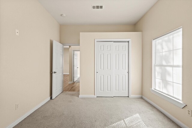 unfurnished bedroom featuring light carpet, a closet, and multiple windows