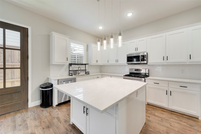 kitchen with white cabinetry, a center island, hanging light fixtures, stainless steel appliances, and light wood-type flooring