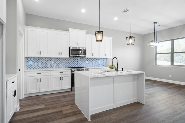 kitchen featuring an island with sink, appliances with stainless steel finishes, decorative light fixtures, dark hardwood / wood-style flooring, and white cabinetry