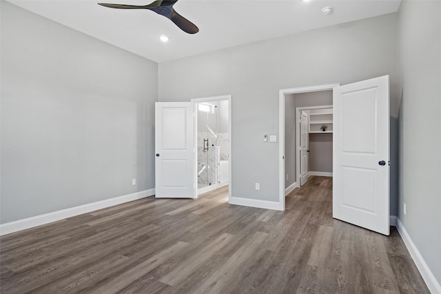 unfurnished bedroom featuring a walk in closet, ensuite bath, ceiling fan, wood-type flooring, and a closet