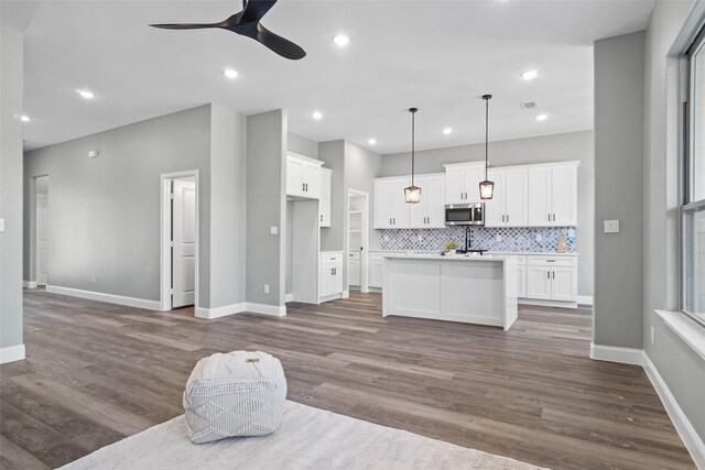 kitchen with backsplash, decorative light fixtures, a center island with sink, dark hardwood / wood-style floors, and white cabinetry