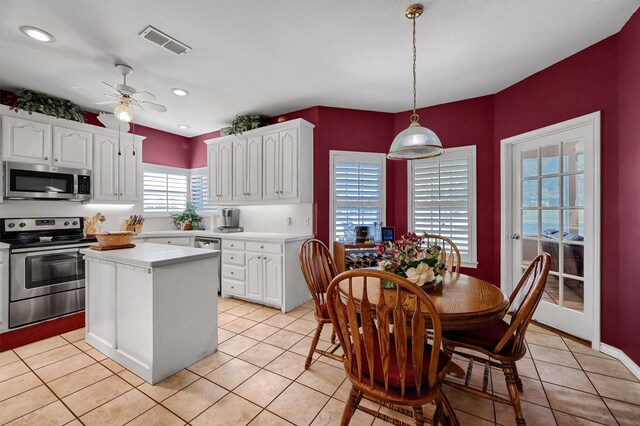 kitchen featuring hanging light fixtures, light tile patterned floors, white cabinets, a kitchen island, and appliances with stainless steel finishes