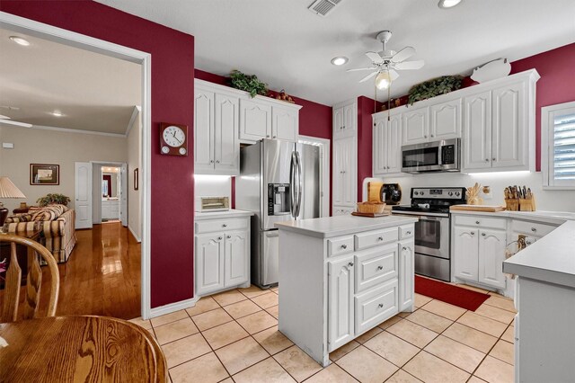 kitchen featuring a center island, ceiling fan, light tile patterned floors, appliances with stainless steel finishes, and white cabinetry