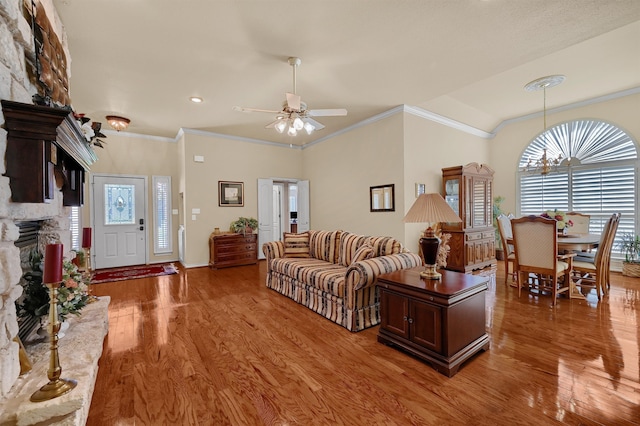 living room with hardwood / wood-style floors, ceiling fan with notable chandelier, a stone fireplace, and crown molding