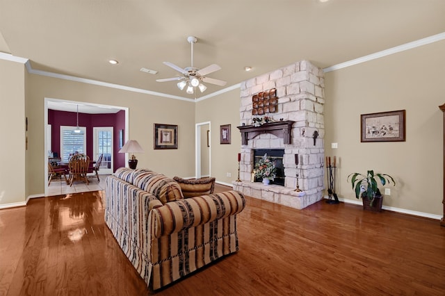 living room with hardwood / wood-style flooring, ceiling fan, a stone fireplace, and ornamental molding