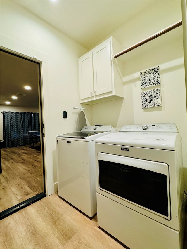 washroom featuring washer and dryer, cabinets, and light hardwood / wood-style flooring