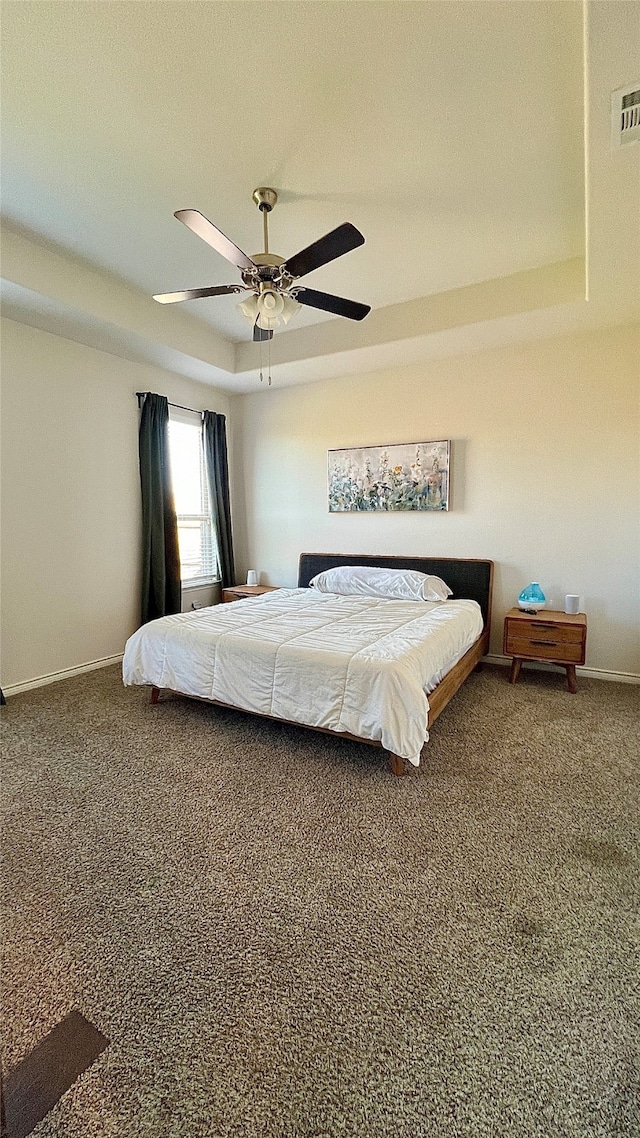 carpeted bedroom with ceiling fan and a raised ceiling