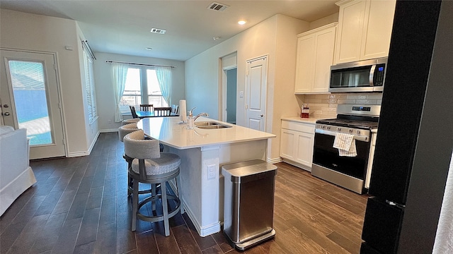 kitchen featuring white cabinetry, sink, dark wood-type flooring, stainless steel appliances, and a center island with sink