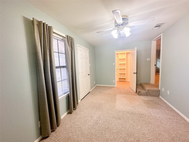 unfurnished bedroom featuring a closet, a walk in closet, light colored carpet, and ceiling fan