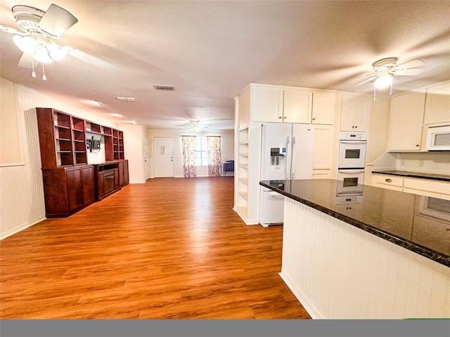 kitchen with white cabinets, light hardwood / wood-style floors, dark stone countertops, and white appliances