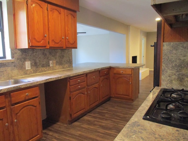 kitchen featuring kitchen peninsula, dark hardwood / wood-style flooring, backsplash, sink, and black gas cooktop