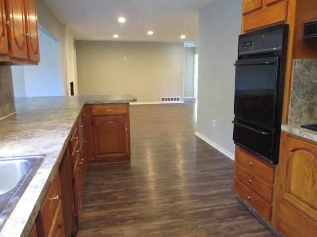 kitchen featuring kitchen peninsula, light stone counters, dark hardwood / wood-style flooring, and decorative backsplash